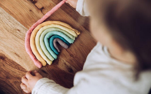 Kleinkind knetet bunten Regenbogen auf Holztisch