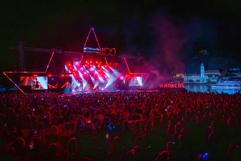 Open-Air-Konzert mit Seebühne und feierndem Publikum bei Sommerabendstimmung in Österreich.