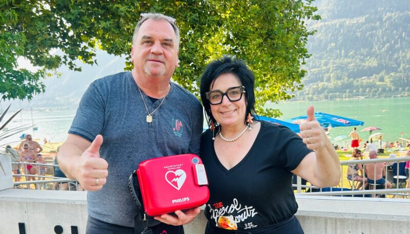 Michaela und und Michael Kopeinig vom Strandbuffet mit dem Defibrillator, der sich zur freien Entnahme im Bereich der Sitztische vor dem Bistro befindet.